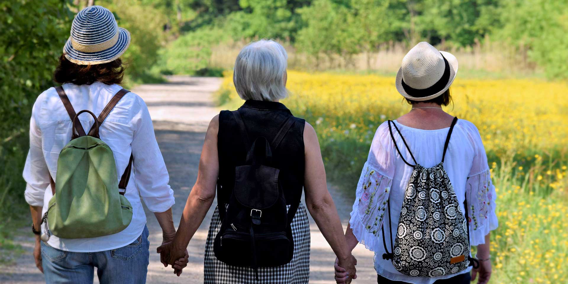 3 Frauen unterschiedlichen Alters spazieren auf einem Wiesenweg