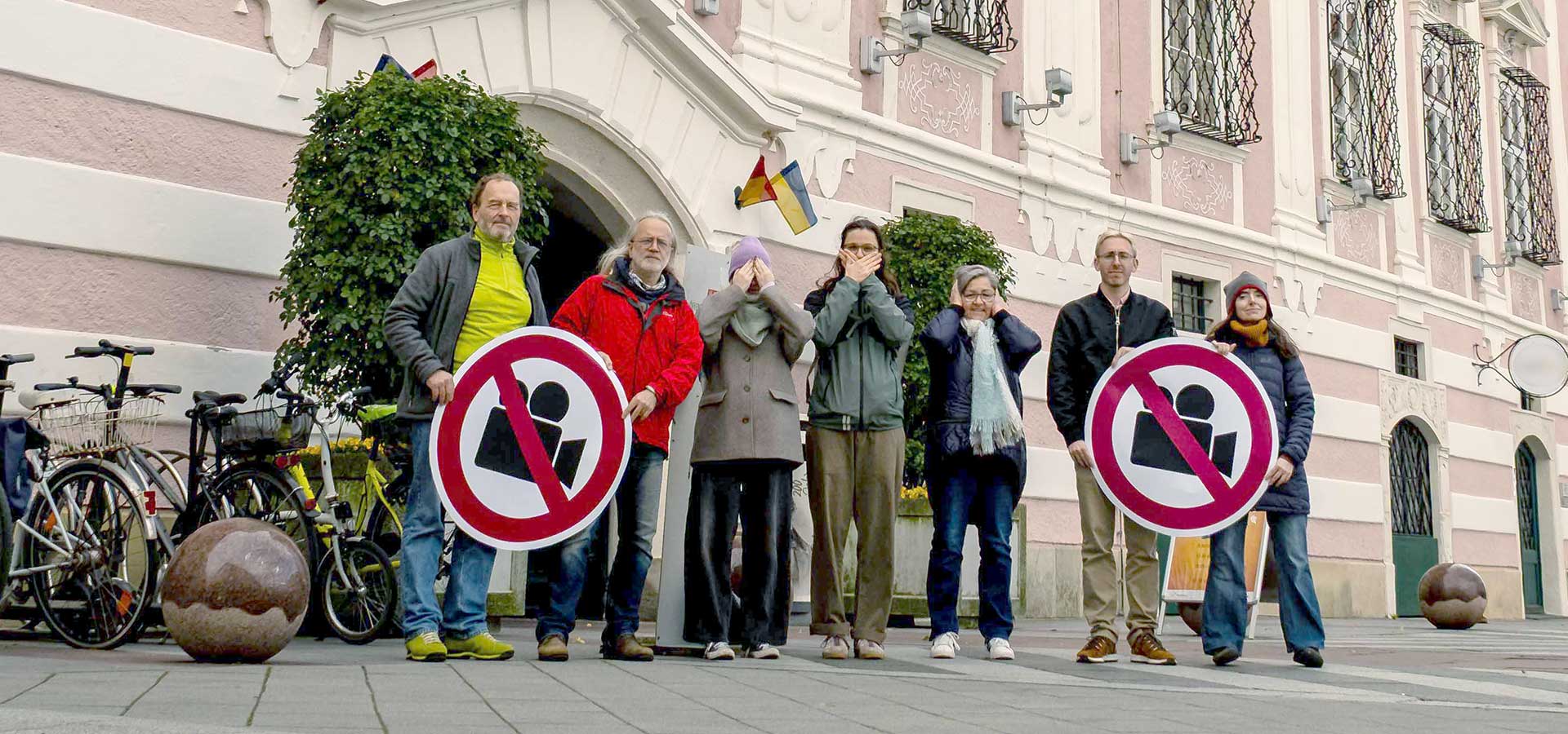 Personen vor dem St. Pöltner Rathaus halten ein Verkehrsschild mit durchgestrichener Videokamera, einzelne halten sich Mund, Augen und Ohren zu