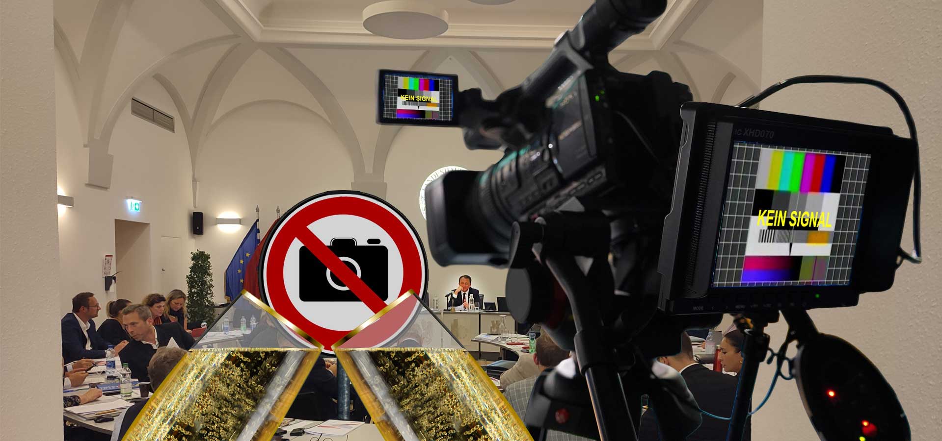 Kamera mit Testbild vor Gemeinderatssitzungssaal mit Schild Kameras verboten, davor 2 Sektgläser