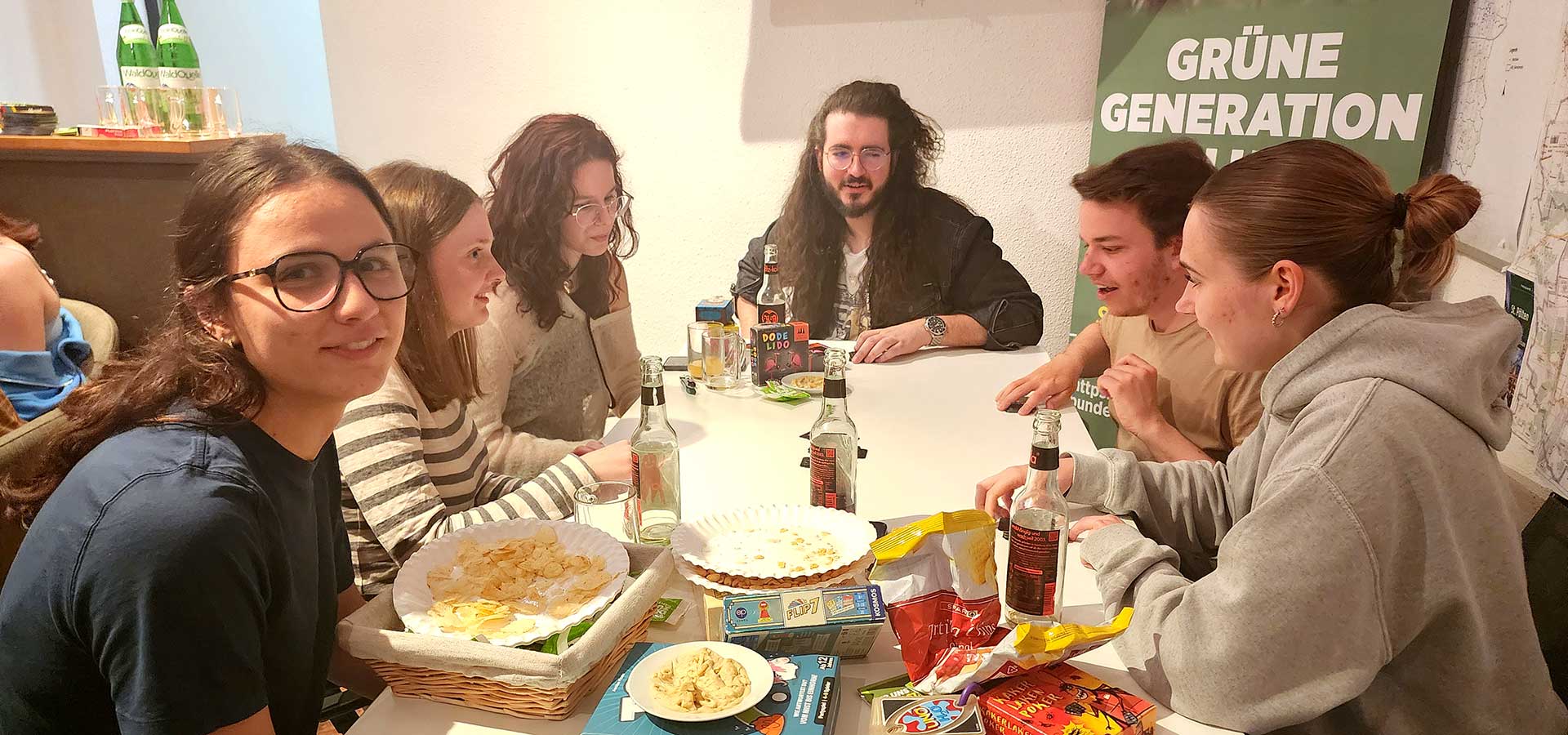 Junge Menschen, versammelt an einem Tisch mit Gesellschaftsspielen, Snacks und Getränken