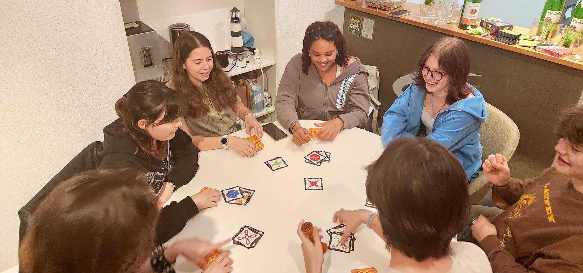 Junge Menschen, versammelt an einem Tisch mit Gesellschaftsspielen, Snacks und Getränken