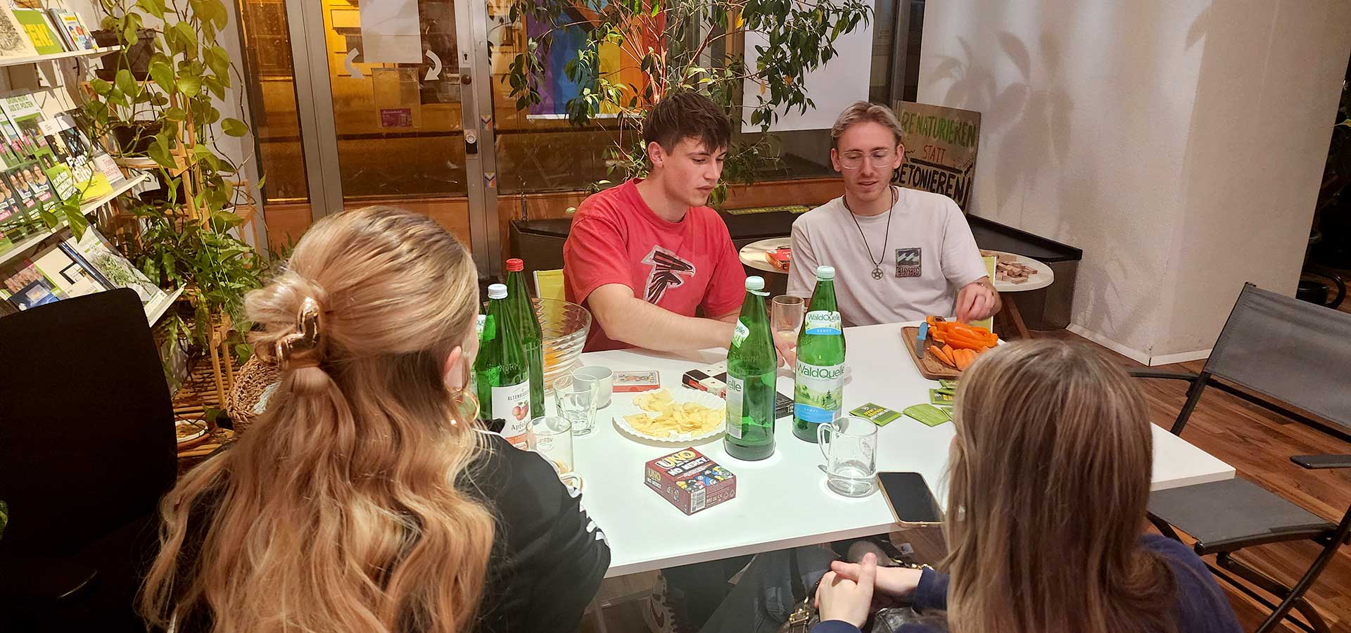 Junge Menschen, versammelt an einem Tisch mit Gesellschaftsspielen, Snacks und Getränken